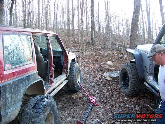 Red off-road SUV with doors removed, next to a silver Jeep Wrangler in a wooded area