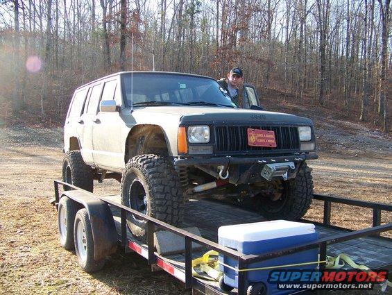 Lifted Jeep Cherokee XJ on a trailer with a man standing in the driver's door