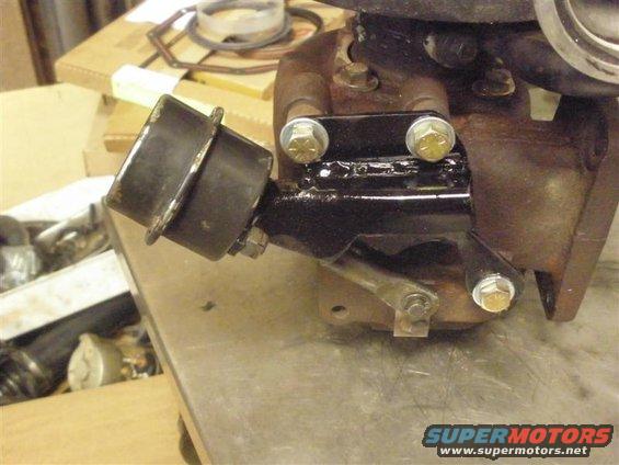 Turbocharger wastegate actuator attached to a black metal bracket bolted to a rusty turbocharger housing