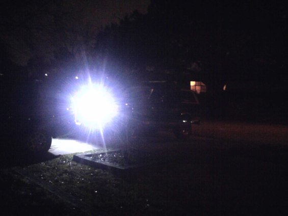 Dark SUV with extremely bright headlights on, angled from the front-left