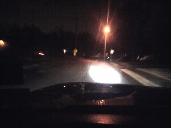 Dashboard view at night, headlights illuminate a wet road with crosswalk