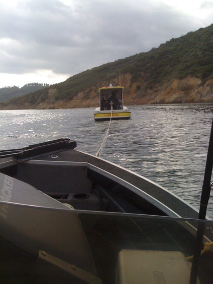 boat being towed by another boat on a lake with a wooded hill in background