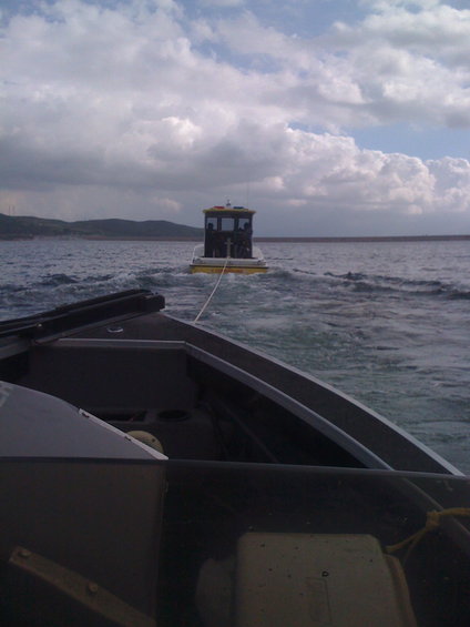 Yellow and white cabin boat being towed by another boat on choppy water under a cloudy sky