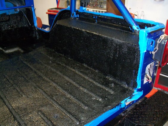 1978 Jeep CJ5 interior bed with black spray-on liner and blue roll cage. Tail light visible on right