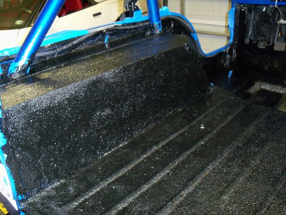 Interior of a vehicle with black textured flooring and blue roll cage. Some blue tape is visible