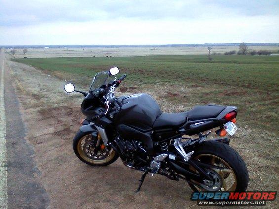 Dark motorcycle parked on a dirt road next to a grassy field