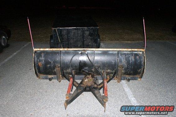 Front view of a snow plow attachment with hydraulic lines and springs. Two pink markers are on top