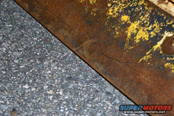 Rusted metal edge with yellow paint flecks over asphalt
