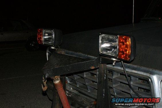 Front view of a truck with aftermarket square headlights and amber turn signals mounted on a custom bracket. Grille visible
