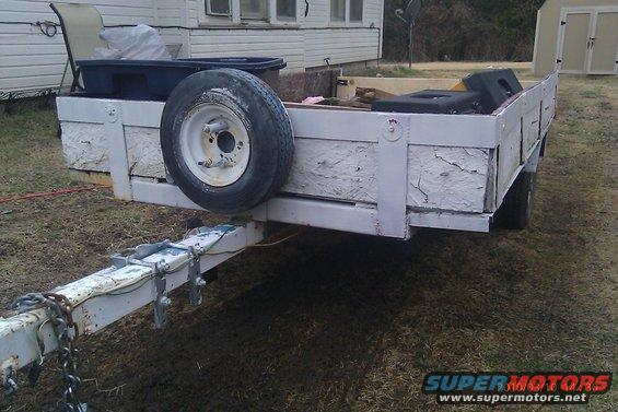 Utility trailer with white painted sides, spare tire mounted on front left, and various items in the bed