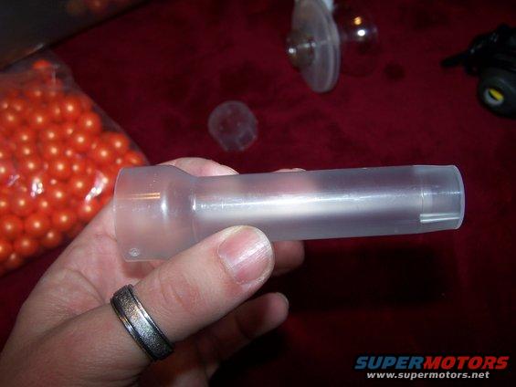 Clear plastic part held in hand, with orange beads in background