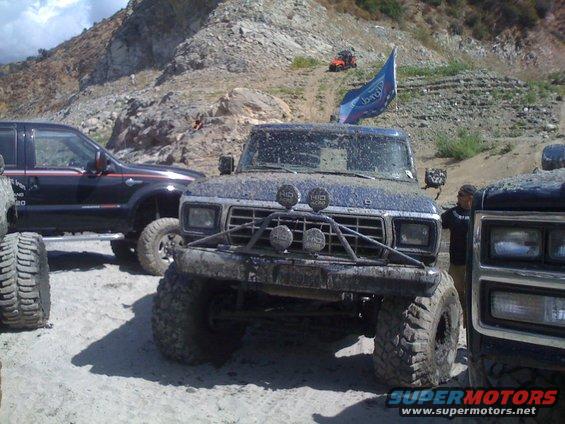 Muddy 1979 Ford Bronco with custom bumper and off-road tires, parked next to another truck