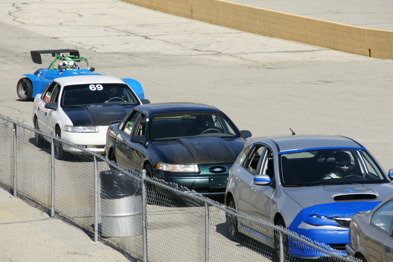 Cars lined up on a track, one has a big spoiler