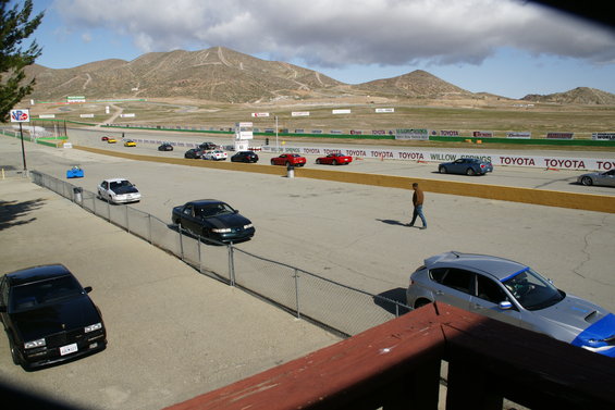 Cars on a racetrack with mountains in the background. A man walks on the track