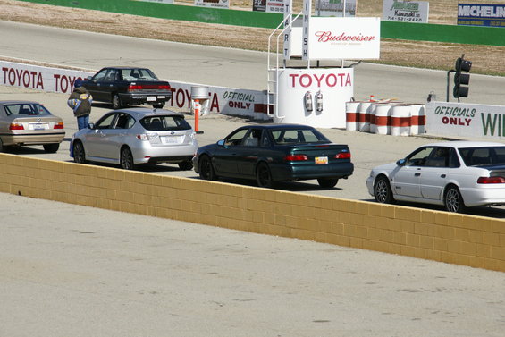Several cars on a race track, including a silver Subaru hatchback and a dark green sedan