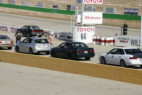 dark green sedan on race track, white sedan behind it