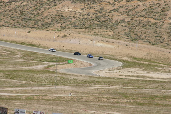 Four cars race on a winding track with dry, hilly terrain