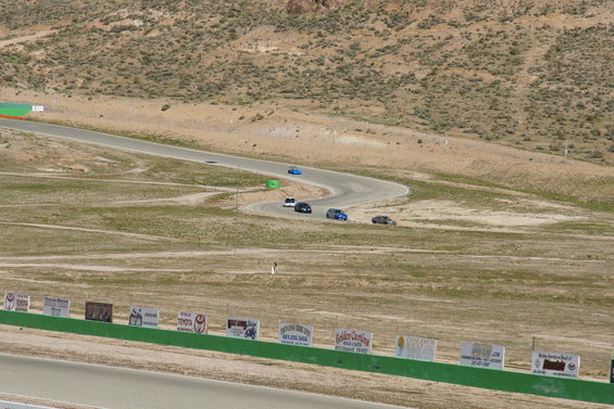 Cars on a winding race track with desert hills and sponsor signs