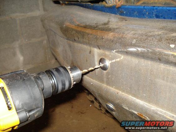 Drill bit making a hole in a rusty bumper. A metal fastener is being installed