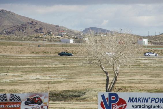 Dark sedan driving on a track, with a white car in the distance