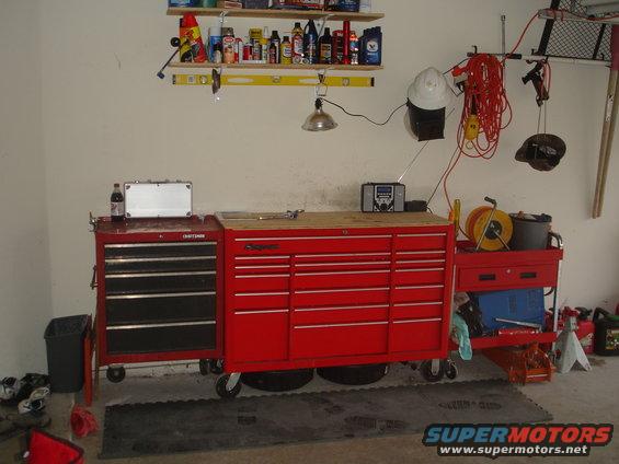 Red Craftsman and Snap-on tool chests with a workbench top, shelves with supplies above, and various garage items around