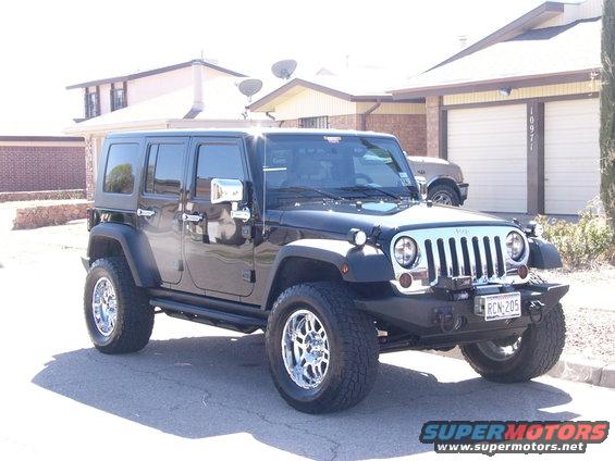 Black four-door Jeep Wrangler parked in driveway. Another SUV is visible in the garage behind it