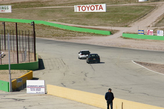 Two cars on a race track, one white and one dark, with a Toyota sign in the background