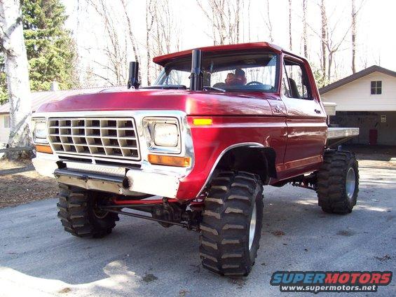 Red lifted pickup truck with large tires, dual exhaust stacks, and a flatbed. Looks like a 1978 Ford F-150