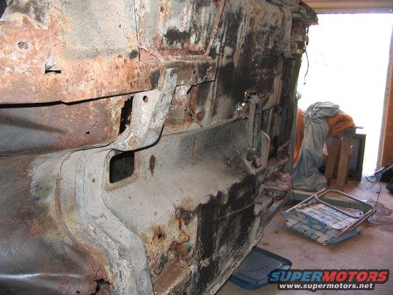 Heavily rusted car frame, possibly a classic, showing significant structural decay. Some parts are detached