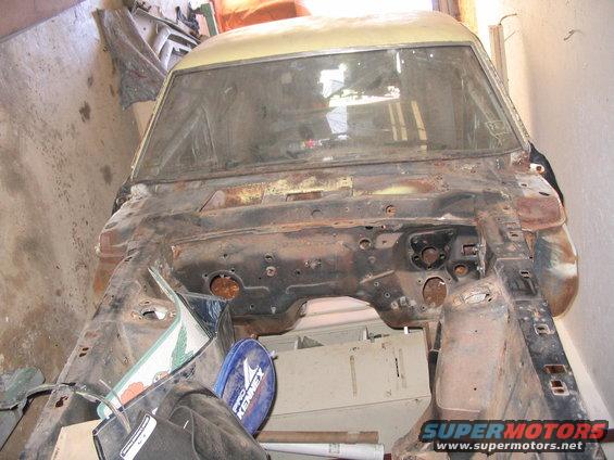 1970 Ford Mustang chassis, front view, showing engine bay and front frame rails. Car is rusty and appears to be undergoing restoration