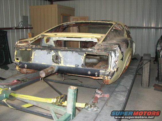 Yellow 1970 Ford Mustang body on a lift, showing rust and missing parts