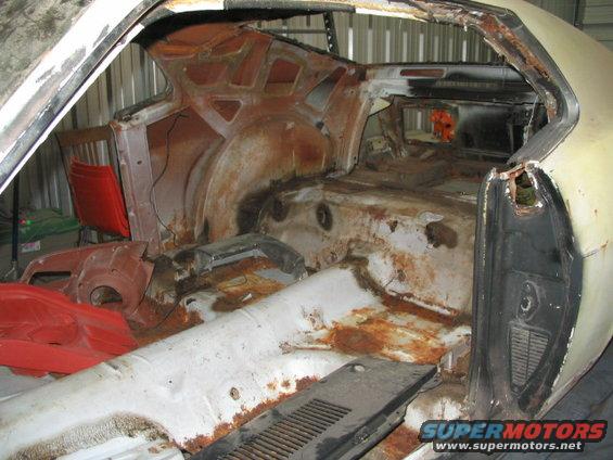 1970 Ford Mustang interior, showing extensive rust and damage to the floor and rear quarter panels