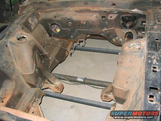 Car frame, looks like the engine bay and front chassis area. It's rusty and appears to be undergoing restoration