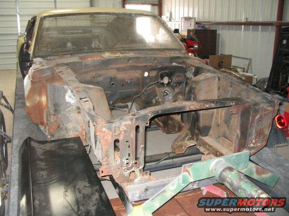 1970 Ford Mustang chassis in a workshop, showing heavy rust and missing engine components