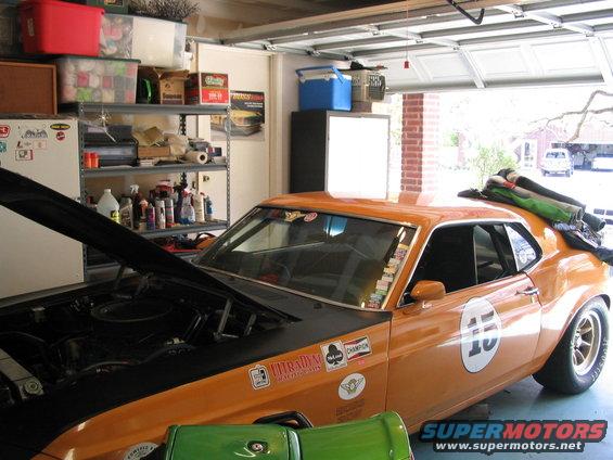 1970 Ford Mustang race car with hood open in a garage, covered in decals