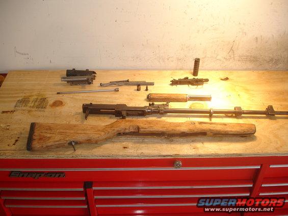 Disassembled firearms laid out on a wooden workbench atop a red tool chest