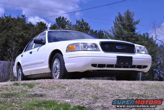 White 2002 Ford Crown Victoria parked on a grassy incline, front 3/4 view