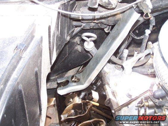 Engine bay with metal bracket, hoses, and valve cover visible