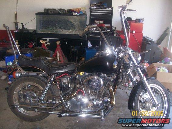 Black custom motorcycle with tall handlebars and sissy bar, parked in a garage