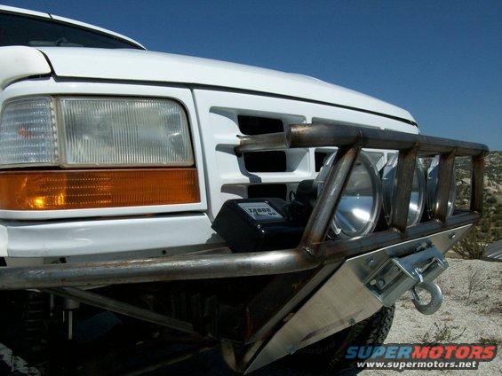 White Ford truck front end with custom metal bumper, winch, and auxiliary lights. Grille indicates 1992-1996 model