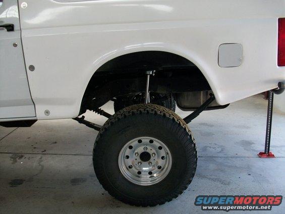 White SUV's rear wheel well and suspension components, with a jack supporting the frame