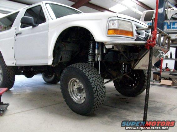 White 1996 Ford Bronco with aftermarket bumper and suspension, being worked on in a garage