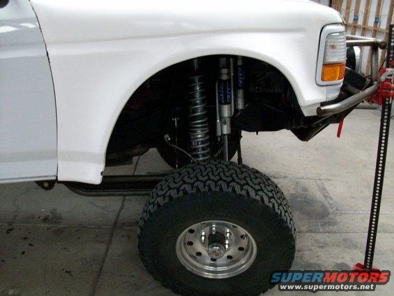 White Ford Bronco front fender, suspension, and tire with a jack beside it