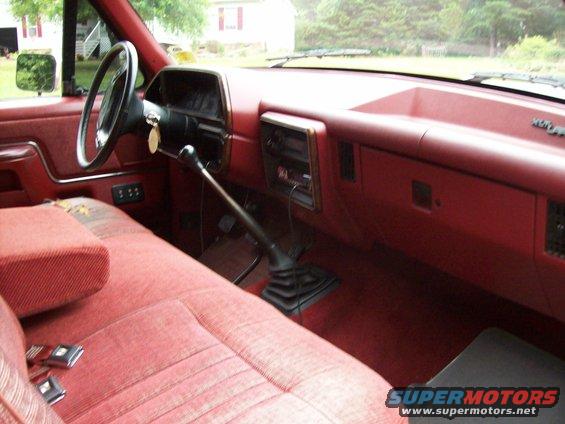 Interior of a 1990 Ford F-150 with red seats and dashboard, manual transmission shifter visible