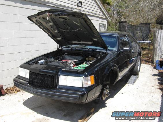 1990 Lincoln Mark VII with hood open, front wheels removed, sitting on ramps