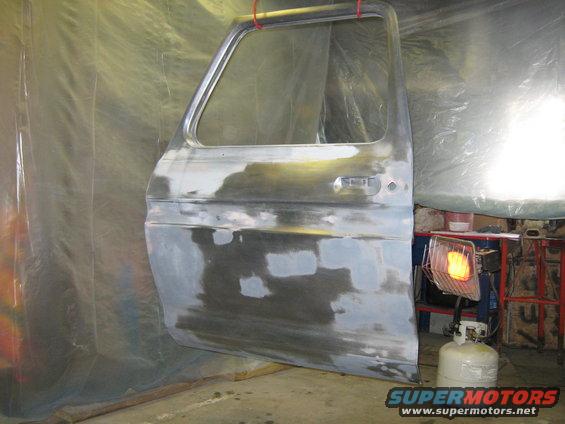Truck door with primer and body filler, hanging from red straps. A propane heater is nearby