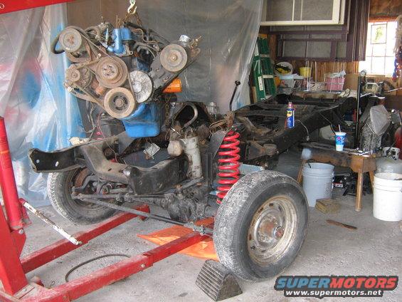 Engine hoisted above a vehicle chassis with red springs and a tire visible