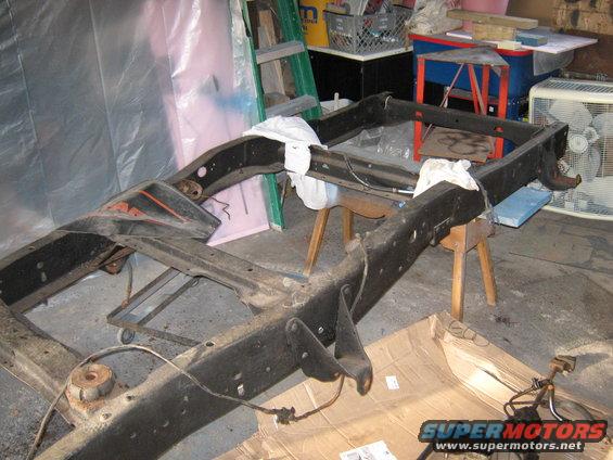 Truck frame on sawhorses in a garage, with tools and a fan in the background