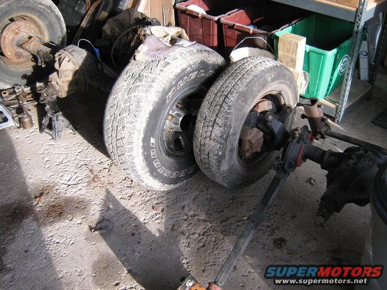 Vehicle axles and tires are on the ground in a workshop. One tire has Bridgestone written on it