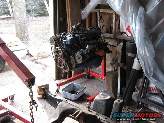 Engine on a red stand in a garage, with a vehicle frame in the foreground